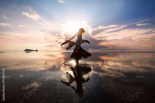Elegant woman dancing on water. Sunset and silhouette.