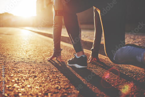 Athlete woman in running start pose on the city street. Sport tight clothes. Bright sunset, blurry background. Horizontal