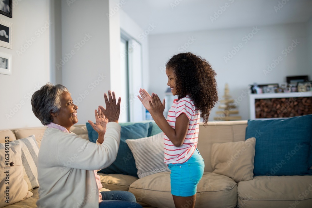 Granddaughter And Grandmother Playing Clapping Games On Sofa In Living