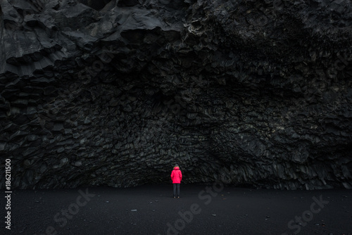 Woman in a red coat stands under Halsanefshellir Cave in Iceland