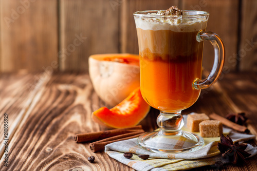 Pumpkin spice latte with whipped cream and cinnamon in glass on rustic wooden background