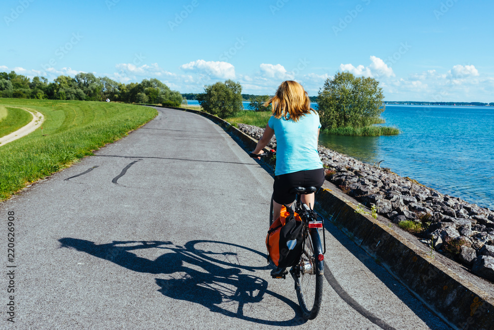 Female Cyclist With Own Shadow On A Bike Path Overlooking Lake And