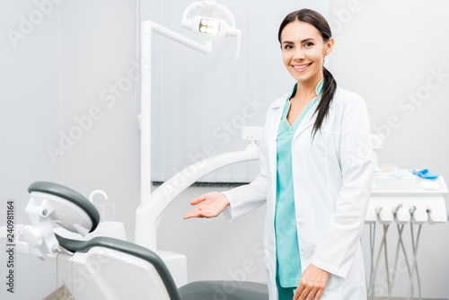 smiling female dentist showing chair in dental clinic