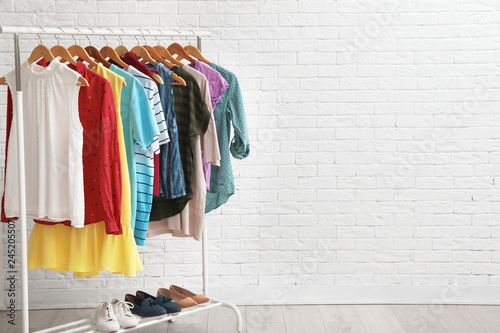 Wardrobe rack with stylish clothes and shoes near brick wall indoors. Space for text