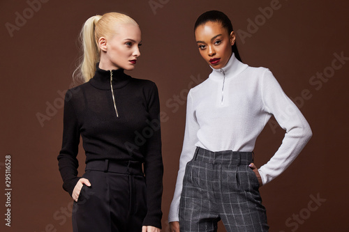 Two beautiful sexy woman long brunette blond hair glamour model wear pants and sweater work office style dress code accessory jewelry studio background fashion party meeting date makeup cosmetic.