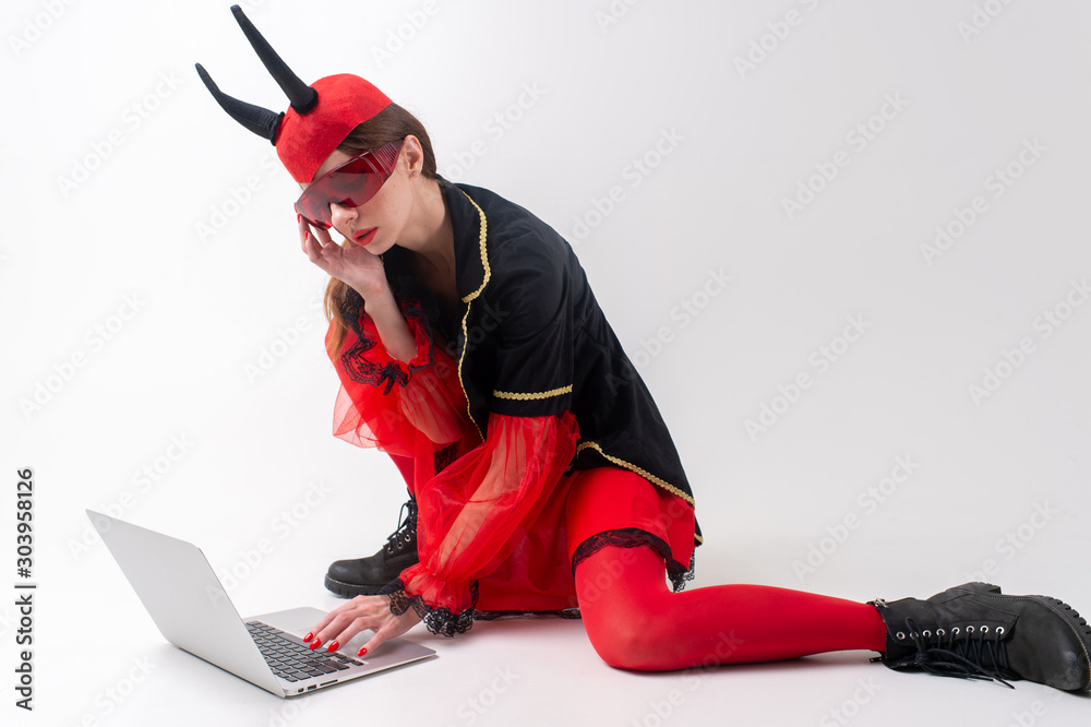 Sexy Brunette Woman In Red Tights Black Boots And Devil Horns Using Laptop Over White Studio
