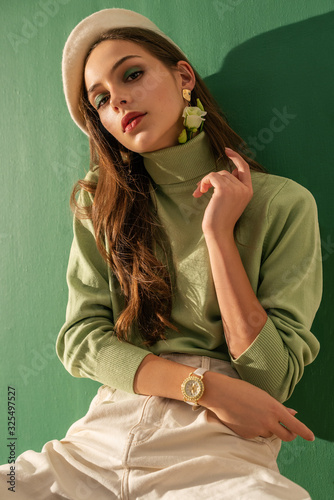 Young beautiful fashionable woman wearing green turtleneck, white beret, wrist watch, posing on mint color background. Spring fashion concept
