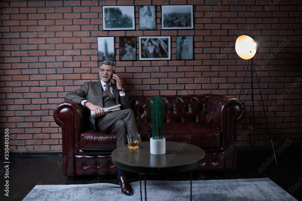 Successful Mature Millionaire In A Business Suit In His Office In The Loft Style Sits On A