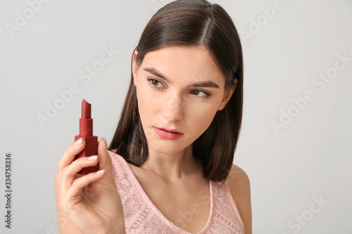 Beautiful young woman applying makeup on light background