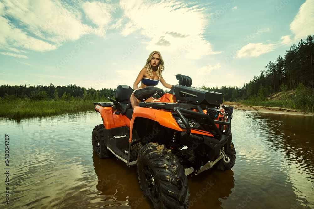 Beautiful Blonde Girl On A Atv Rides On Water And Sand Mountains Green Forest All Around In