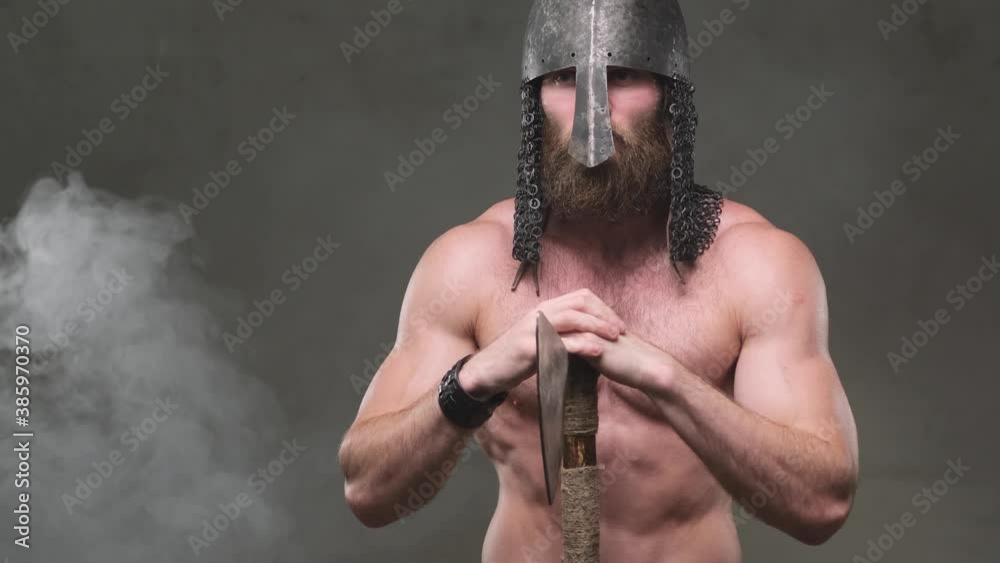 Naked Scandinavian Viking Warrior With Muscular Build And Helmet Stays And Poses With Axe In