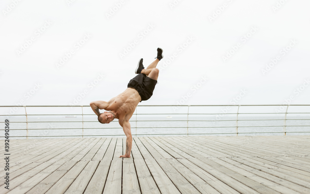 Muscular Bodybuilder Fitness Man With A Naked Torso Stands On One Arm On The Beach Stock Photo