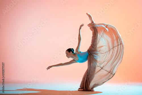 Ballerina in a light dress is dancing on colored background with backlight