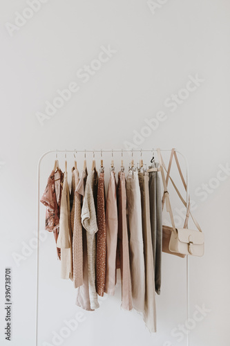 Women's fashion pastel clothes. Stylish female blouses, sweaters, pants, jeans, t-shirts, handbags on hanger on white background. Minimalist fashion blog.