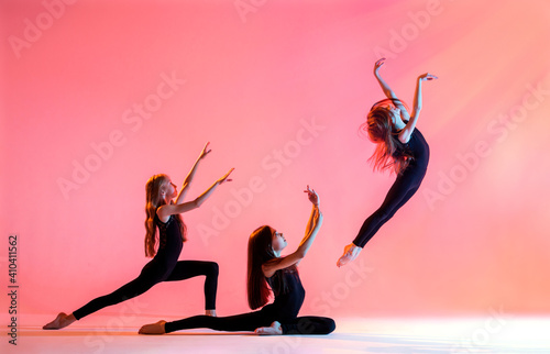 group of three ballet girls with long flowing hair in black tight-fitting suits dance on red background