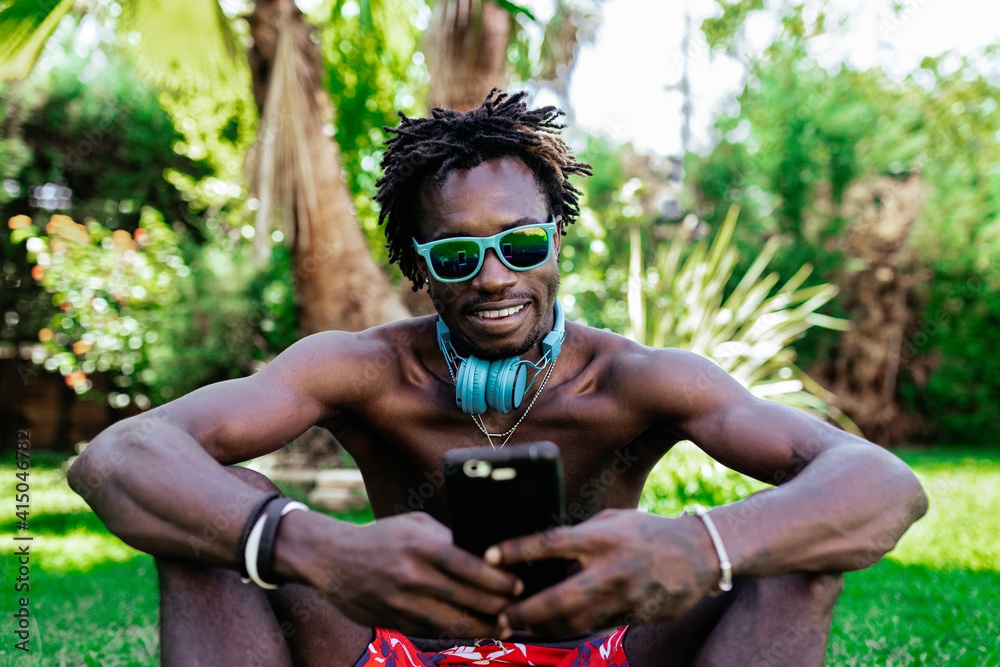 Content African American Male With Naked Torso And In Sunglasses Sitting On Meadow In Park And