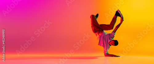 Flyer with young stylish man, break dancing dancer training in casual clothes isolated over gradient pink yellow background at dance hall in neon light.