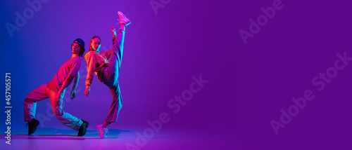 Flyer. Two dancers, young man and woman dancing hip-hop in casual sports youth clothes on gradient purple pink background at dance hall in neon light.