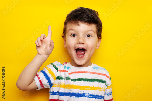 idea. child, boy emotionally points up. A gesture of an idea. Portrait of a child in a bright striped T-shirt on a yellow background