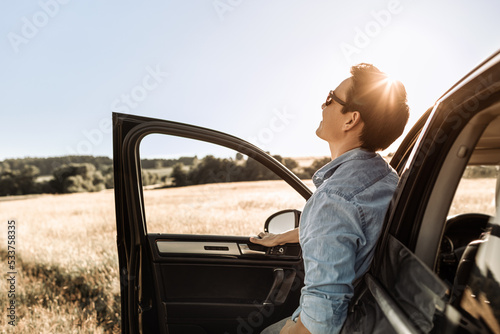 Happy young man getting out of his car looking up to the sky enjoying a beautiful nature view. Happiness and adventure 