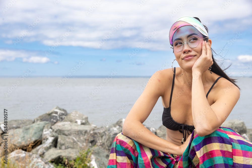 Woman In Bikini On The Beach Wearing A Visor And Colorful Pants Her Hand Is Resting On Her Chin