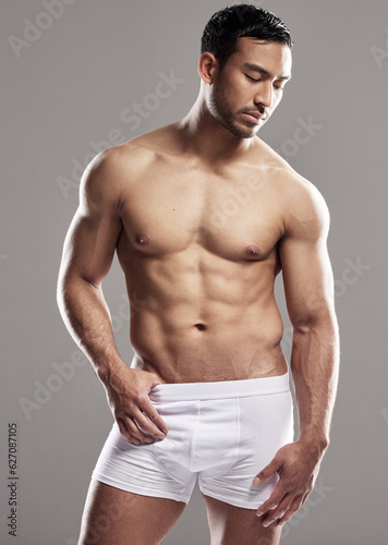 Man, underwear model and body muscle with strong chest, abs and confidence in studio. Bodybuilder, exercise and healthy hot male person with gray background and muscles from fitness and workout