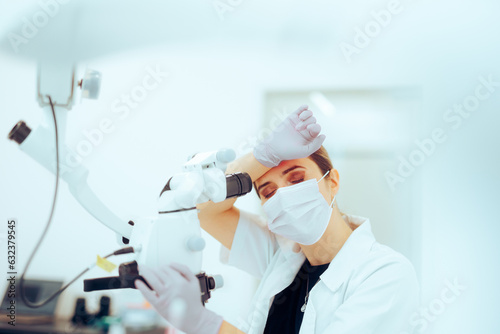 Tired Scientist Feeling Concerned Looking through the Microscope Unhappy doctor doing microsurgery being tired at work 
