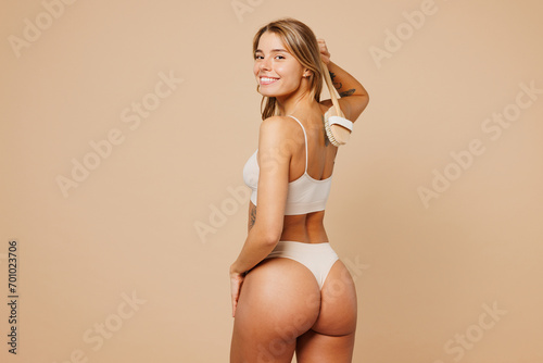 Back rear view young nice lady woman with slim body perfect skin wears nude top bra lingerie stand do scrubbing massage with dry brush isolated on plain beige background. Lifestyle diet fit concept.