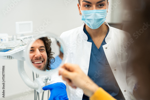 Shot of a young man checking his results in the dentist's office. Proud female dentist and satisfied male patient at dental clinic.
