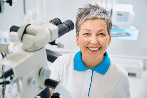 Woman aesthetic dentist spending time in her office with modern microscope