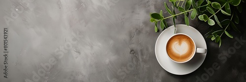 a cup of coffee with a heart on it next to a plant on a table with a gray background