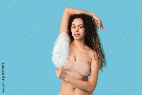 Beautiful young woman with feather on blue background. Depilation concept