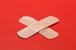 Two crossed adhesive bandages on red background