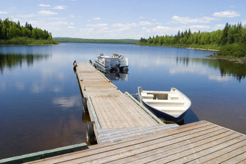 dock with two boats tied to its side on a calm lake surrounded by trees in Canada