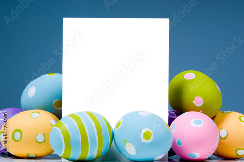 Photo brightly colored easter eggs surrounding white, blank notecard