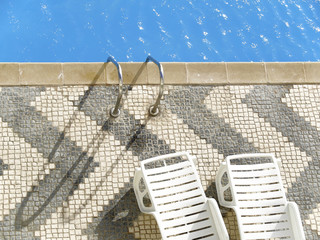 Top view of a swimming pool with two empty white deckchairs.