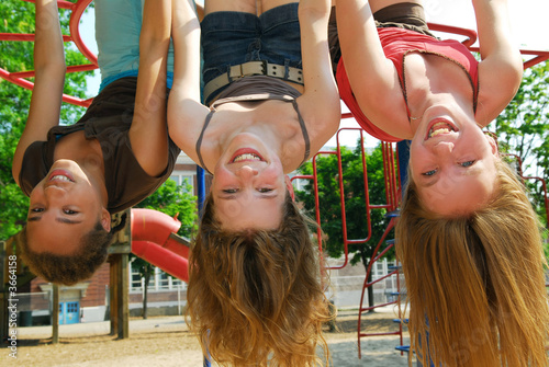 Fotografía Three young girls hanging upside down in a park and laughing