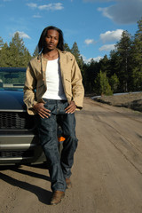 A handsome young man sitting on the hood of his car 