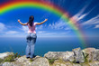 young woman with arms wide open contemplating the rainbow over t