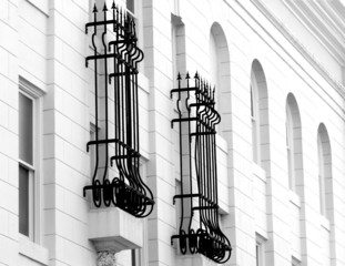 B&W image of wrought iron around two windows of a white building