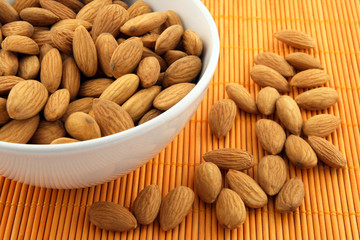 Bowl of almonds on rattan mat of warm orange color.