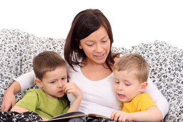 mother and two sons reading book in bed