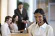 © carlosseller - Young businesswoman on headset with seated colleagues behind