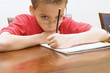Left handed young boy wearing glasses reluctant to do homework