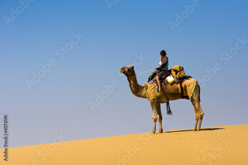 Fotografia, Obraz Riding a camel on a sand dune - Thar desert, Rajasthan, India