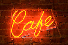 A Neon Sign On A Brick Wall Outside Of A Cafe