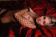 very sexy young woman in fishnet body suit on red satin bed