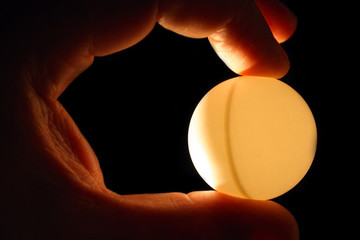 Wall Mural - mans hand hold ball ping pong against light isolated on black