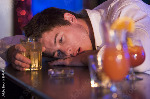 Fotografering Drunk young man resting head on bar counter