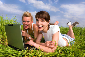 Wall Mural - Two beautiful girls are laughing near laptop computer outdoors